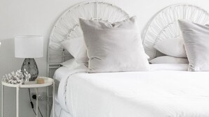 Un lit avec une tête de lit blanche, une table de chevet avec une lampe et un petit objet décoratif posé sur la table.