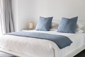 A neatly made bed with a white headboard, two pillows, a blue throw blanket, and a bedside lamp.