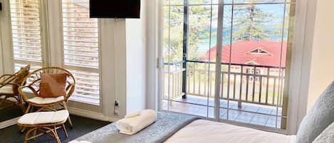 A hotel room with a bed, two chairs, a TV, and a balcony with a red-roofed building view.