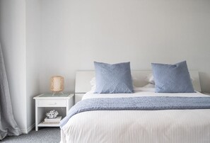 A bedroom with a bed, two pillows, a nightstand with a lamp, and a decorative item on the nightstand.