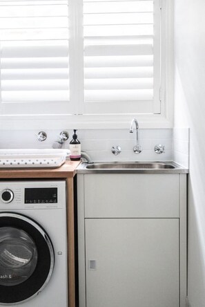 A compact kitchen with a washing machine, a sink, and a window with blinds.