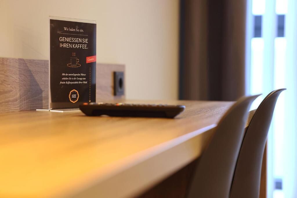 A wooden table with a black object on it, a sign with text in German, and a chair in the foreground.