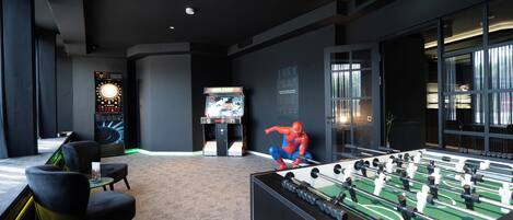 Una habitación con una mesa de fútbol de mesa, un televisor de pantalla grande y una estatua de Spider-Man.