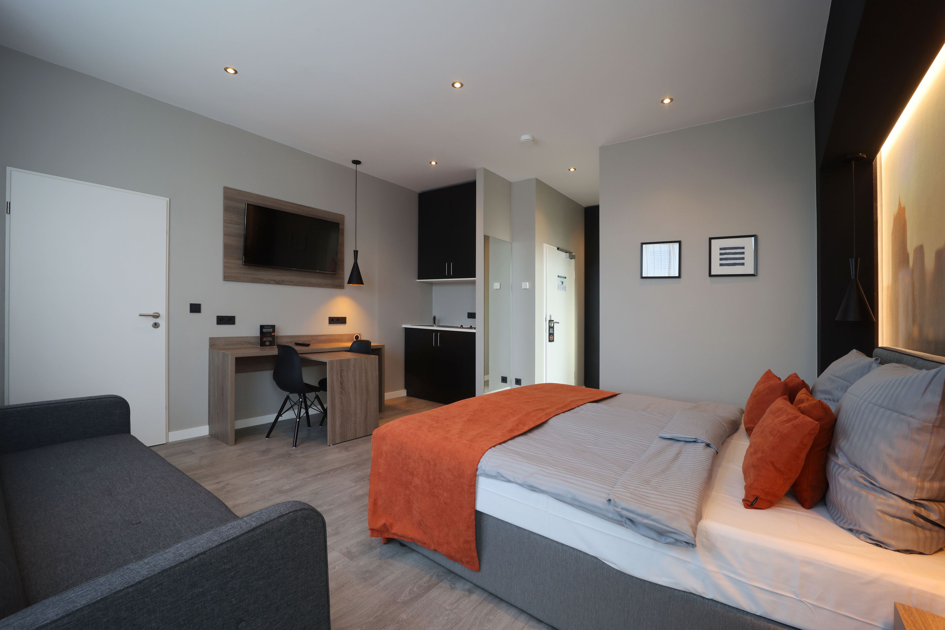 Een moderne hotelkamer met een bed, een bureau, een stoel en een aan de muur bevestigde televisie.