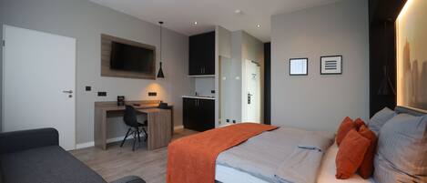 A modern hotel room with a bed, a desk, a chair, and a TV mounted on the wall.