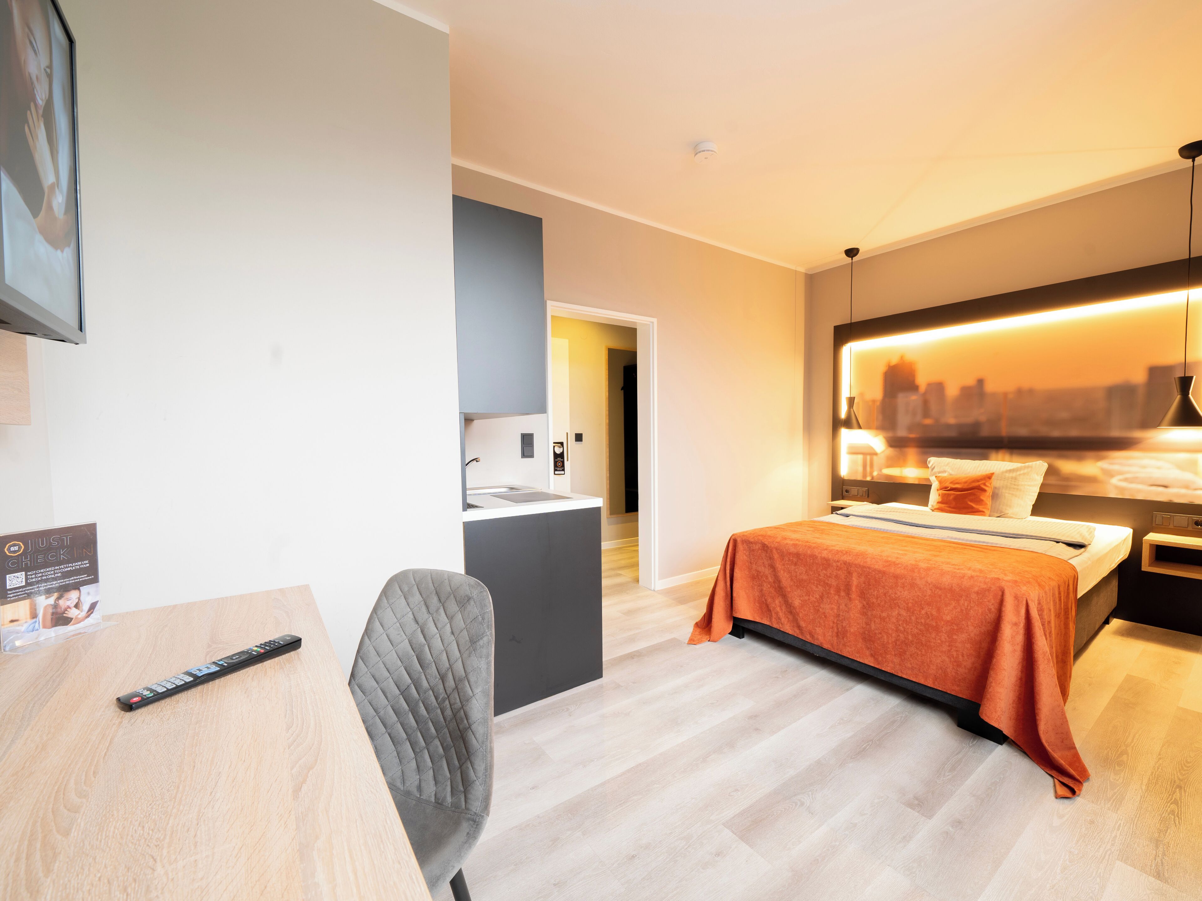 Habitación de hotel moderna con cama, escritorio, silla, kitchenette y vistas a la ciudad.