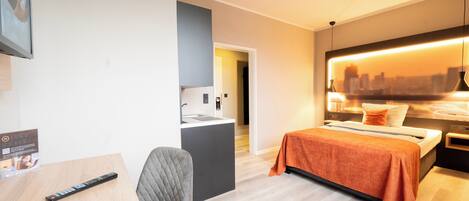 Habitación de hotel moderna con cama, escritorio, silla, kitchenette y vistas a la ciudad.