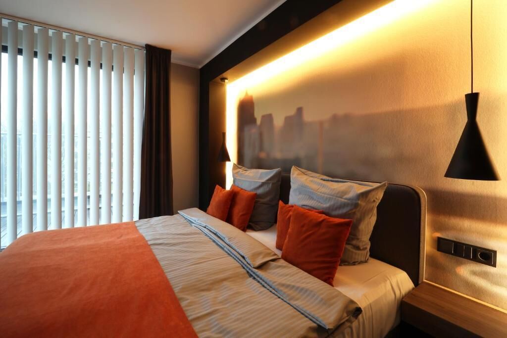 Un hotel moderno con una cama grande, una obra de arte con temática urbana en la pared y vistas a la ciudad desde la ventana.