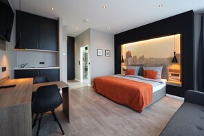 A modern bedroom with a bed, a desk, and a view of a cityscape through a large window. - JustStay Mülheim/Oberhausen Hotel & Apartments (Muelheim an der Ruhr)