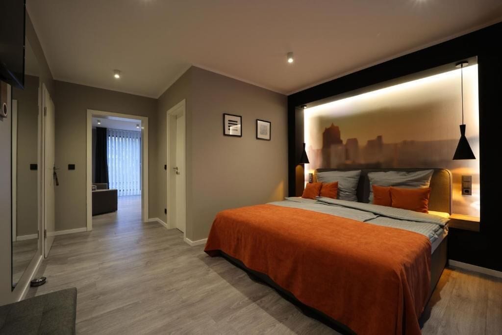 A modern bedroom with a large bed, a cityscape wall art, and a hallway leading to another room.
