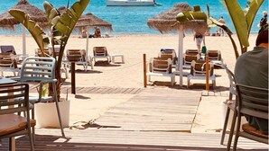 A beachside patio with lounge chairs and thatched umbrellas, overlooking the sea and a sailboat. - Wow☀️☀️☀️☀️☀️ Beachfront apartment, panoramic views, amazing sunsets, XL pool! (Marbella)