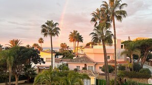 A residential area with palm trees, a garden, and a building with a tiled roof. - Wow☀️☀️☀️☀️☀️ Beachfront apartment, panoramic views, amazing sunsets, XL pool! (Marbella)
