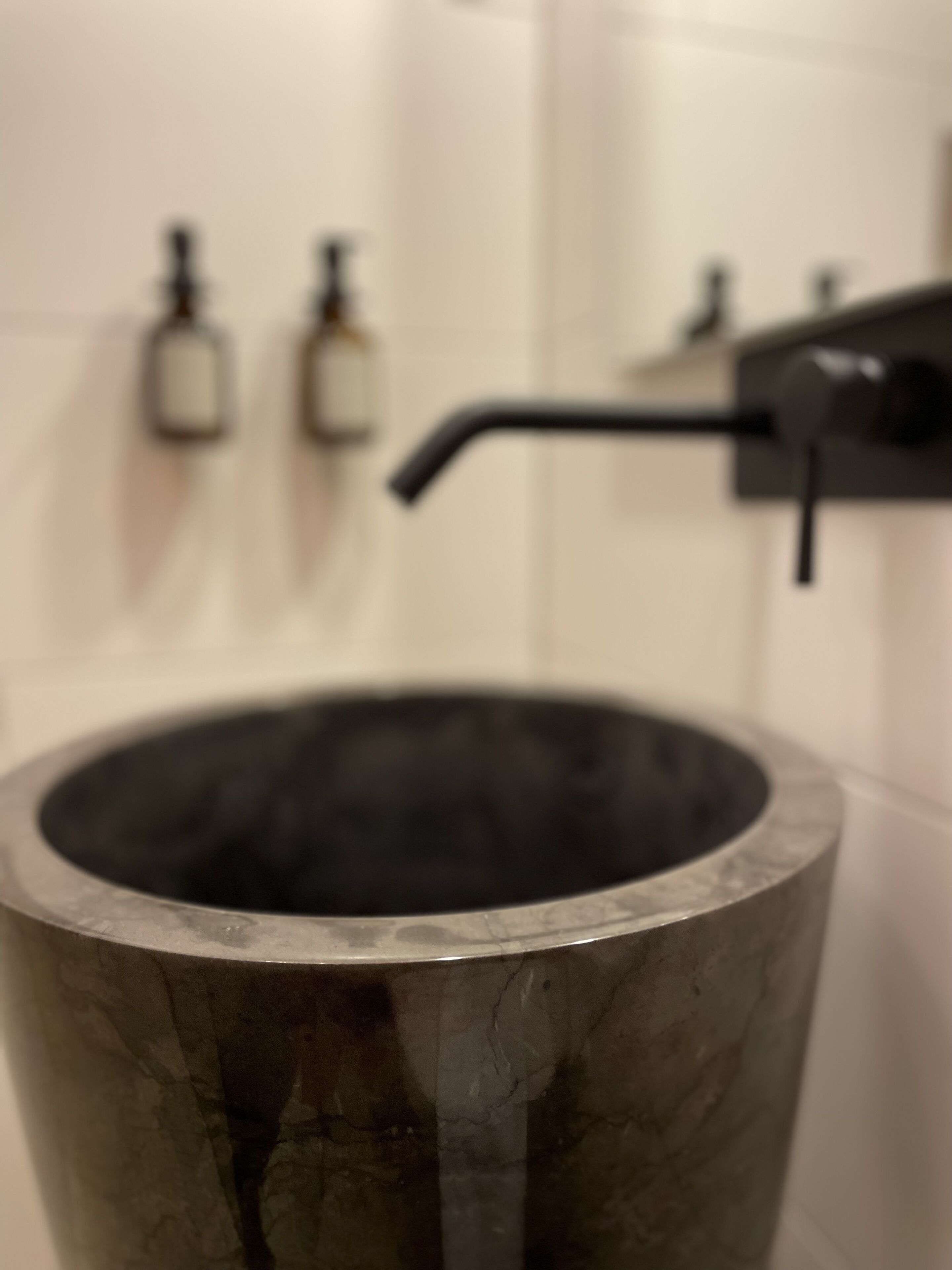 Ett badrum med ett stort badkar i mörk färg, en handduksställning och två tvålpumpar på väggen.