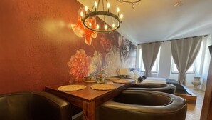 A dining area with a wooden table, black leather chairs, a chandelier, and a floral mural on the wall. - Boutique Apartment Vino e Amore (Freiburg im Breisgau)