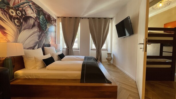 A hotel room with a large bed, a TV mounted on the wall, and a decorative wall mural. - Boutique Apartment Vino e Amore (Freiburg im Breisgau)