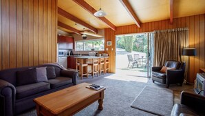 A cozy living room with a sofa, coffee table, and a dining area with a kitchen in the background. - 1970's Renovated, self contained comfortable 2 bedroom bach (Wanaka)