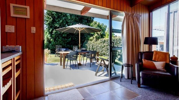 A room with a sliding glass door leading to an outdoor patio with a table, chairs, and an umbrella. - 1970's Renovated, self contained comfortable 2 bedroom bach (Wanaka)