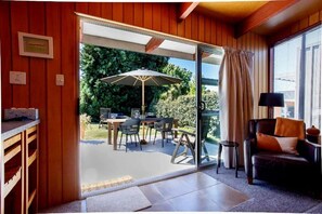 A room with a sliding glass door leading to an outdoor patio with a table, chairs, and an umbrella. - 1970's Renovated, self contained comfortable 2 bedroom bach (Wanaka)