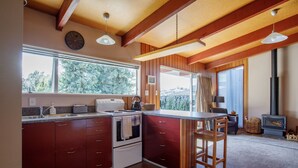 A kitchen with wooden cabinets, a stove, a sink, and a window overlooking a forest. - 1970's Renovated, self contained comfortable 2 bedroom bach (Wanaka)