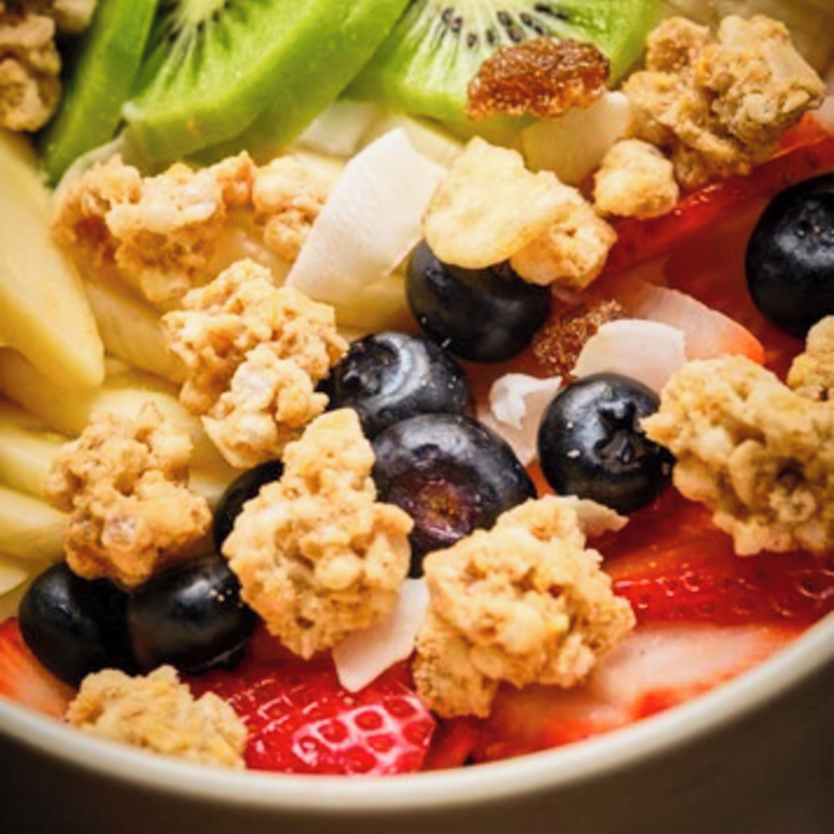 Une salade de fruits composée de fraises, de myrtilles, de kiwis et de granola.