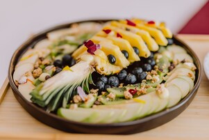 A fruit platter with sliced apples, bananas, blueberries, and nuts on a dark plate.