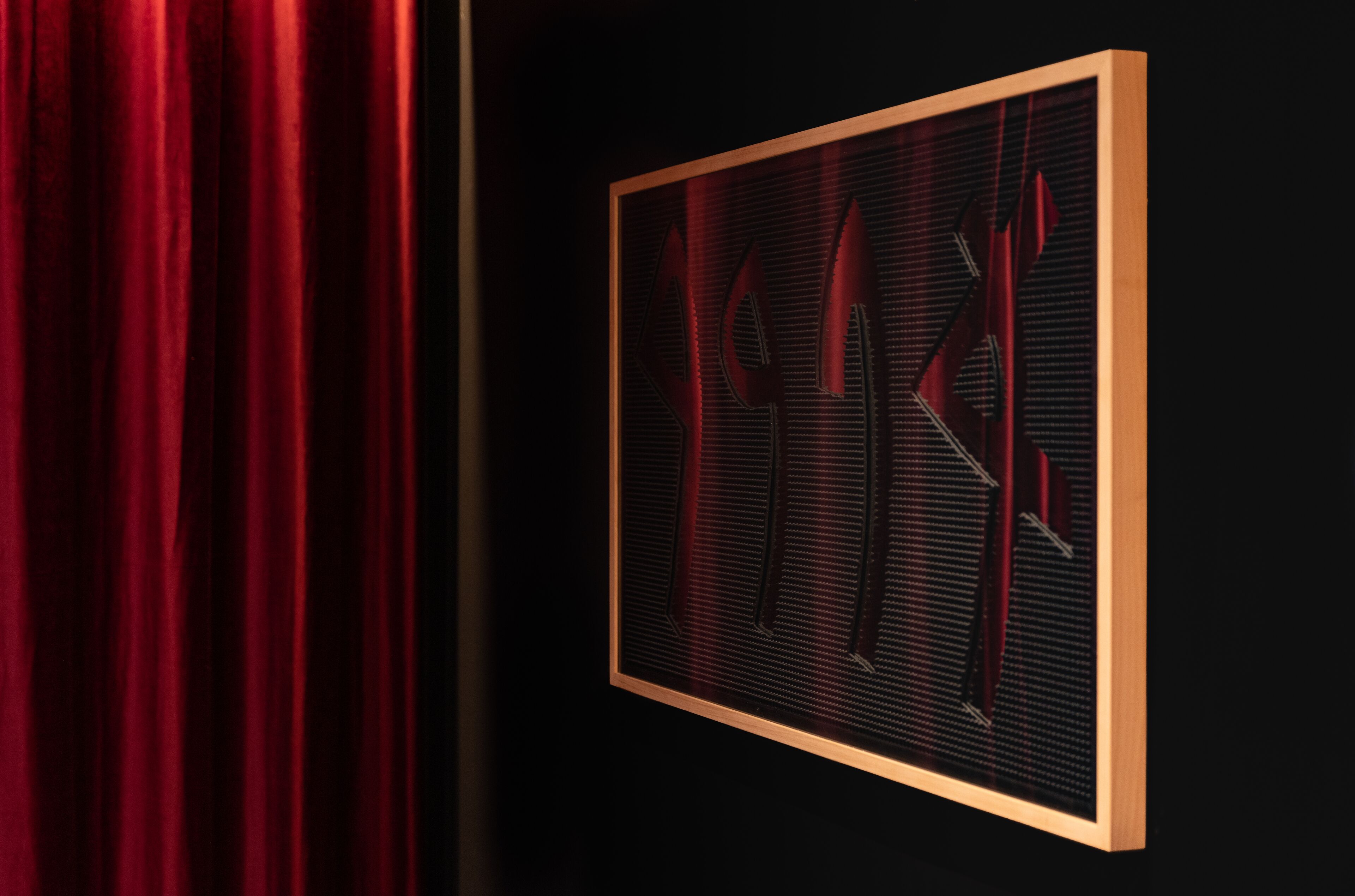 Una obra de arte enmarco con formas abstractas y una cortina roja al fondo.