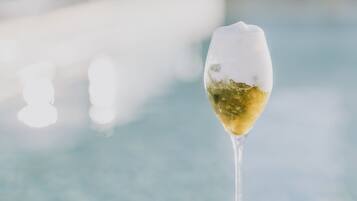 Una copa de vino blanco sobre una superficie blanca cerca de una piscina.