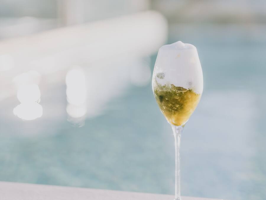 Una copa de vino blanco sobre una superficie blanca cerca de una piscina.