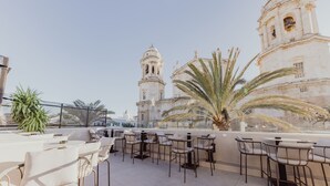 Terraza en la azotea con mobiliario exterior y vista a un edificio histórico con una torre campanario.