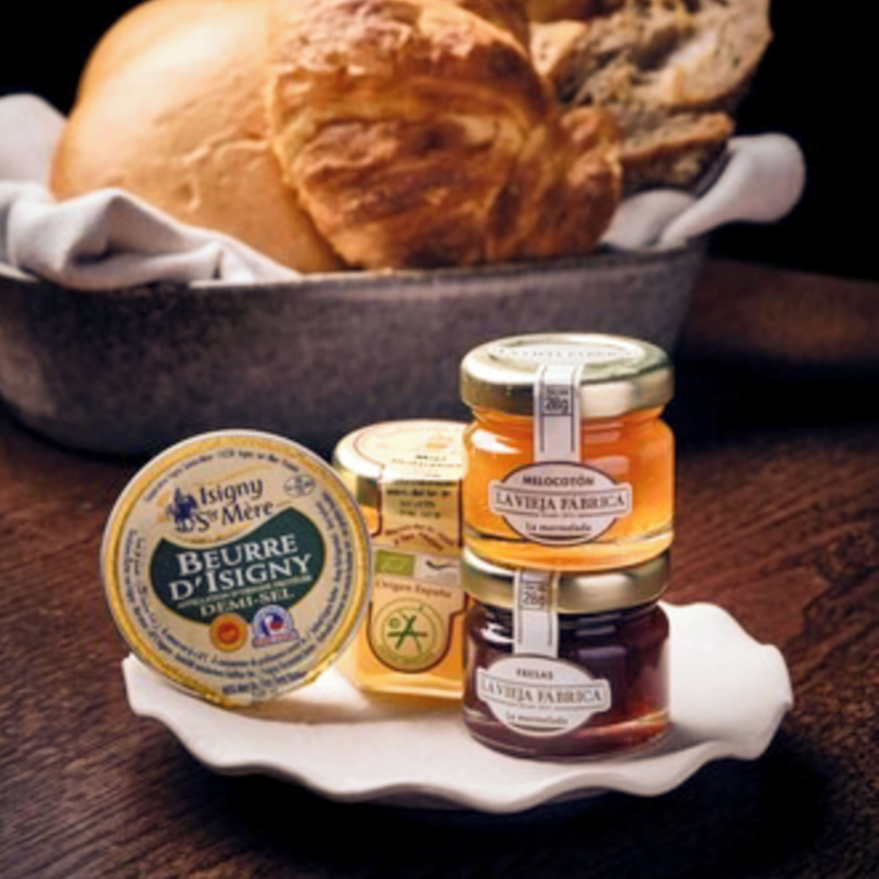 A jar of honey, a jar of jam, and a round container of butter on a white plate.