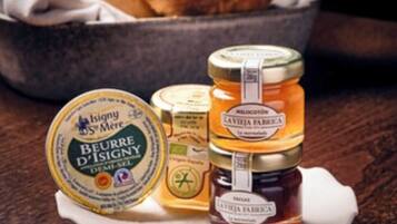 A jar of honey, a jar of jam, and a round container of butter on a white plate.