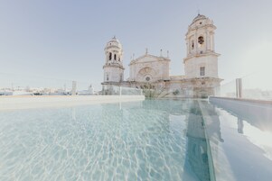 A rooftop pool with clear water, overlooking a historic building with two bell towers.