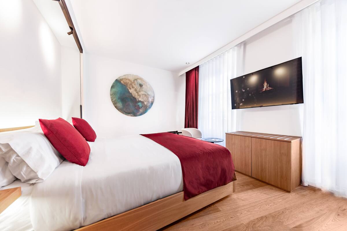 A modern hotel room with a wooden bed, a flat-screen TV, a round artwork on the wall, and a wooden side table.