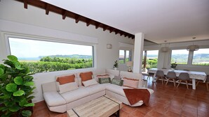 Una sala de estar moderna con un sofá seccional grande, un comedor con mesa y sillas, y amplios ventanales que ofrecen una vista panorámica.