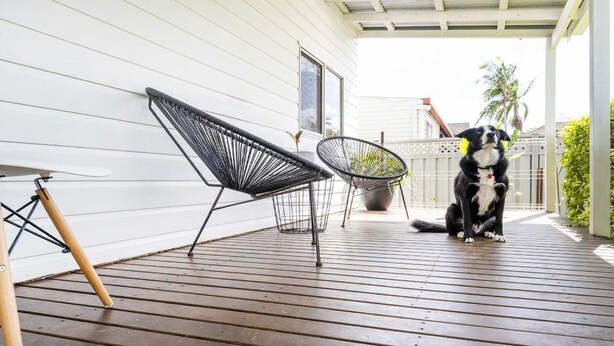 Een houten terras met twee zwarte, metalen stoelen en een bloempot.