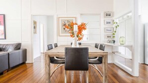 Een eetruimte met een houten tafel, zwarte stoelen en een witte vaas met oranje bloemen.