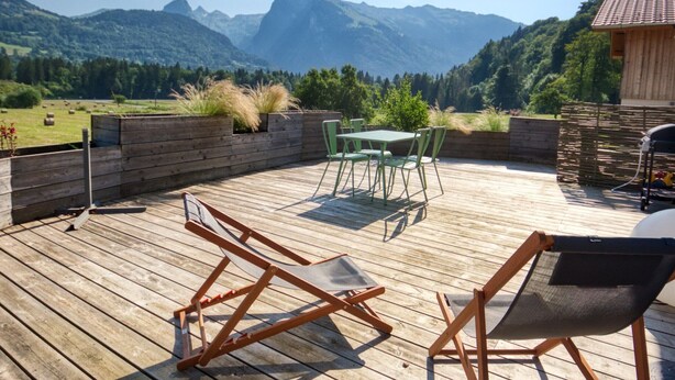 A wooden deck with outdoor furniture, a view of mountains, and a wooden building. - Quiet 2-bedroom apartment with terrace in Samoëns (Samoëns)