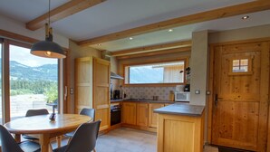 A modern kitchen with wooden cabinets, a dining table with chairs, and a view of mountains through large windows. - Quiet 2-bedroom apartment with terrace in Samoëns (Samoëns)
