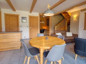 Ein Essbereich mit Holztisch und -stühlen, eine Küche mit Holzschränken und eine Treppe, die zu einer weiteren Ebene führt.