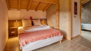 A bedroom with a wooden ceiling, a bed with white bedding, a red throw blanket, and a nightstand with a lamp. - Quiet 2-bedroom apartment with terrace in Samoëns (Samoëns)