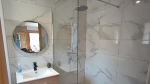 A modern bathroom with a glass-enclosed shower, marble tiles, a round mirror, and a wooden vanity with drawers. - Quiet 2-bedroom apartment with terrace in Samoëns (Samoëns)