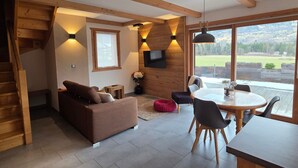 A modern interior with a wooden staircase, a sofa, a dining table with chairs, and a TV mounted on the wall. - Quiet 2-bedroom apartment with terrace in Samoëns (Samoëns)