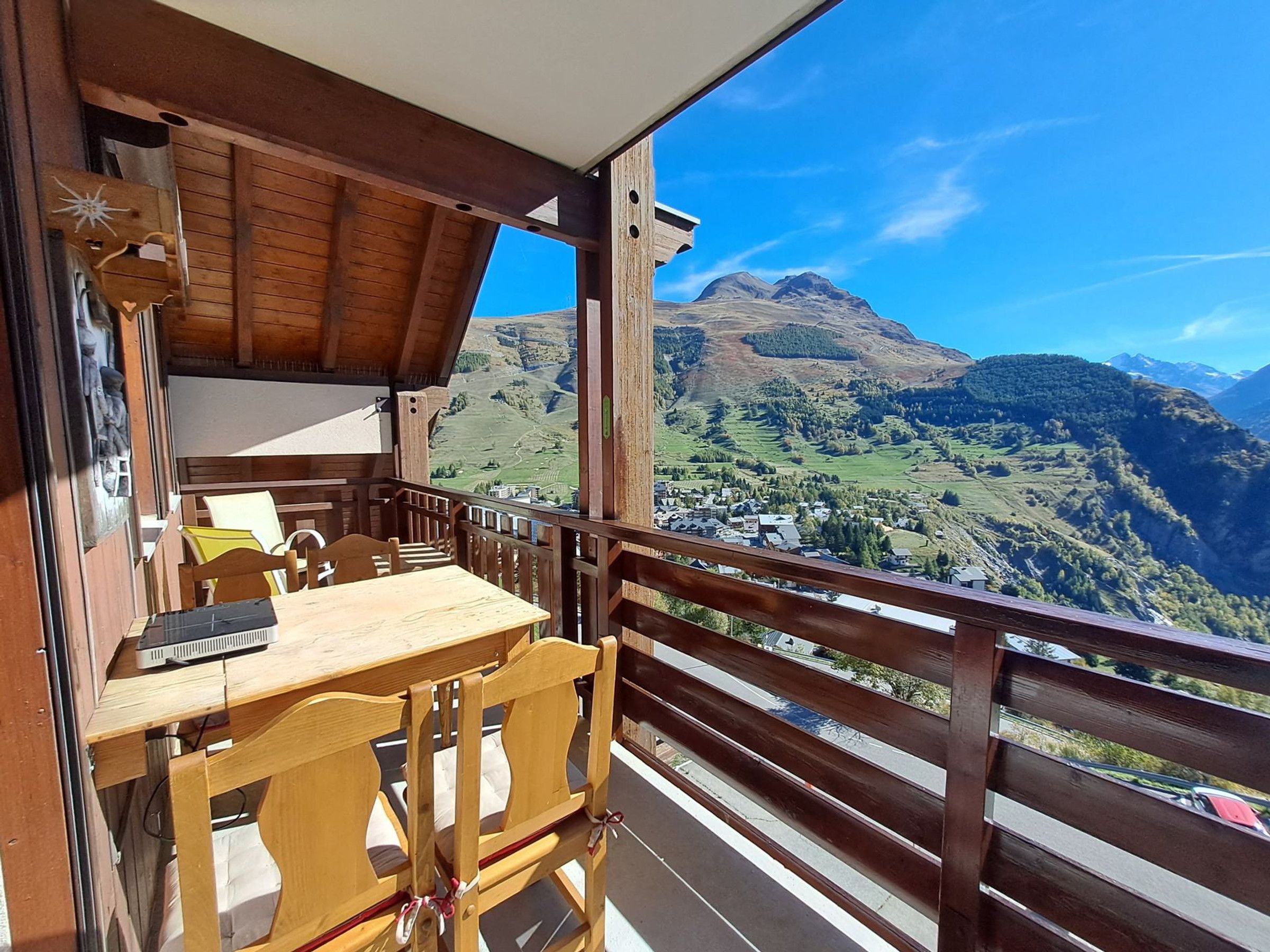 Een houten balkon met een tafel en stoelen, met uitzicht op een bergachtig landschap.