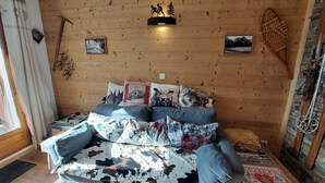 A cozy room with a wooden wall, a sofa with patterned cushions, and a mounted picture of a mountain scene. - Charming T3 with view, close to slopes, pets allowed, covered parking (Les Deux Alpes)