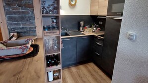 A compact kitchen with dark cabinets, a Bosch refrigerator, a wooden shelf with wine bottles, and a clock on the wall. - Charming T3 with view, close to slopes, pets allowed, covered parking (Les Deux Alpes)