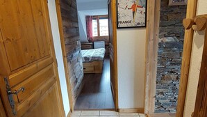 A narrow hallway leading to a bedroom with a bed, a poster on the wall, and a stone wall. - Charming T3 with view, close to slopes, pets allowed, covered parking (Les Deux Alpes)