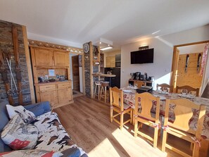 A cozy room with a wooden dining table, chairs, a sofa, and a kitchen area with a TV.