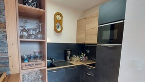 A compact kitchen with dark cabinets, a Bosch microwave, a wooden shelf with wine glasses, and a mirror on the wall. - Charming T3 with view, close to slopes, pets allowed, covered parking (Les Deux Alpes)