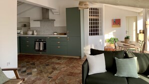 A cozy living room with a dark green sofa and a coffee table, a kitchen with green cabinets and a stone backsplash, and a dining area with a table and chairs. - Magnificent apartment with terrace and rooftop view (Aix-en-Provence)