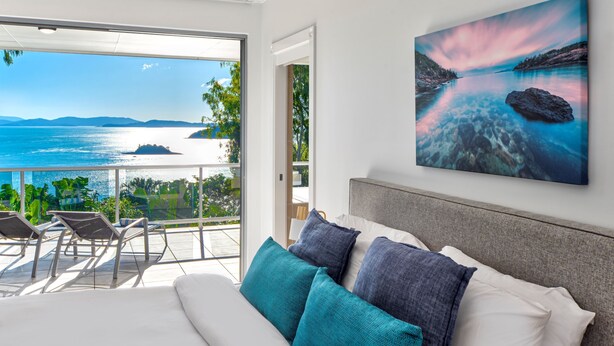 A bedroom with a large bed, a view of the sea, and a balcony with chairs.